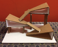 Photo showing the side of Anna's structure, a multi-level object made of cardboard consisting of three triangular prisms connected by cardboard strips.