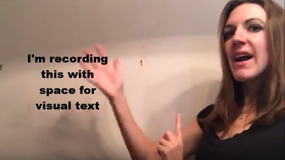 This figure shows me (a young woman with medium-length brown hair wearing a black shirt) rotating my right hand around visual text in the space to my right that reads, in black font, &ldquo;I'm recording this with space for visual text.&rdquo;