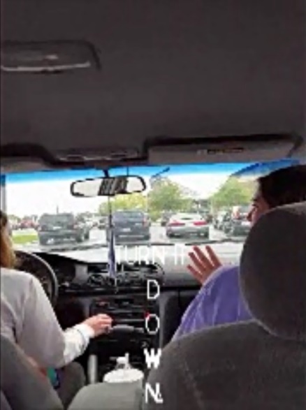The camera is in the backseat of a car in the middle seat to show the front row of the car from the back. Two young women are seated in the front seats and looking at each other, so only their profiles are seen. The driver has her hand on the radio button as captions appear at the top of the screen. The captions read &ldquo;TURN IT DOWN&rdquo; in white capitalized letters and the word &ldquo;DOWN&rdquo; appears as a vertically written word. Each letter in the word DOWN appears alone so that the viewer&rsquo;s eye will go down the screen to read the word.