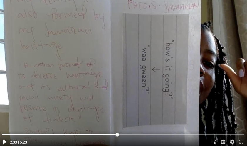 In this photo, Zoey shows two pages from her zine. On the left page, she writes, 'My identity is also formed by my Jamaican heritage. A nation proud of its diverse heritage and its cultural and racial variety will present its identities of dialects. Students' Rights to their Own Language.' On the right zine page, she writes 'Patois-Jamaican' above an English phrase 'How's it going?' translated into Patois: 'waa gyaan?'